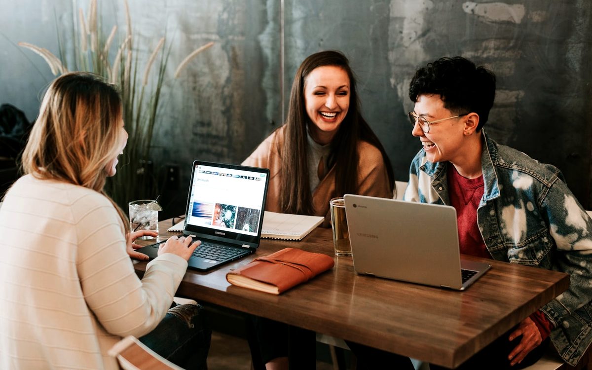 Drie collega's die achter hun laptops overleggen aan een tafel